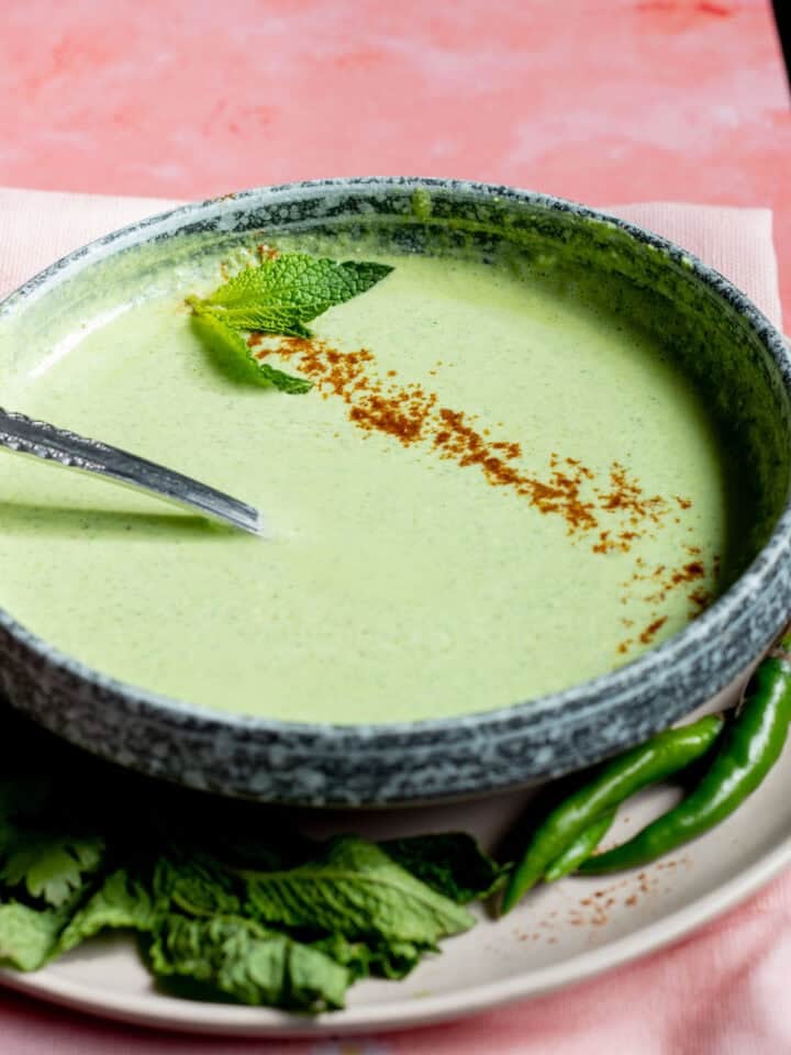 green chutney raita in a bowl garnished with a little cumin powder and mint leaves