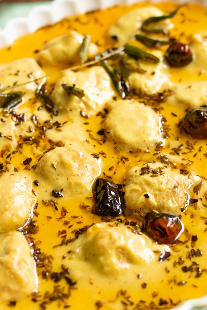 Close-up of Kadhi Pakora, an Indian dish featuring a yellow Karhi curry with dumplings, garnished with dried red chilies, curry leaves, and cumin seeds, all floating in a layer of spiced oil.