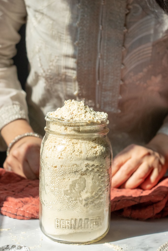 a jar of pakora mix on a counter, a cloth and a person in the background