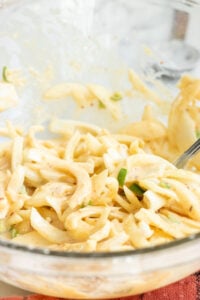 A close-up of a glass bowl filled with creamy coleslaw made of sliced cabbage and green peppers, coated in a mayonnaise-based dressing-perfect as a crunchy side or even as inspiration for How to Make Pakoras with a twist. A metal fork rests in the mixture.