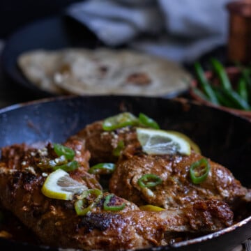 two cooked pieces of tawa chicken in a pan, roti in the backrgound