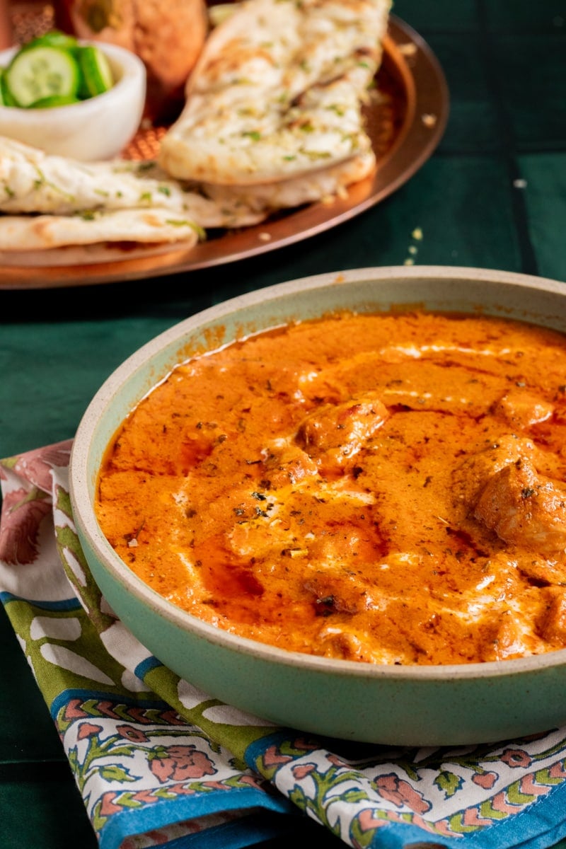 a dish of chicken handi, plate with naan in background