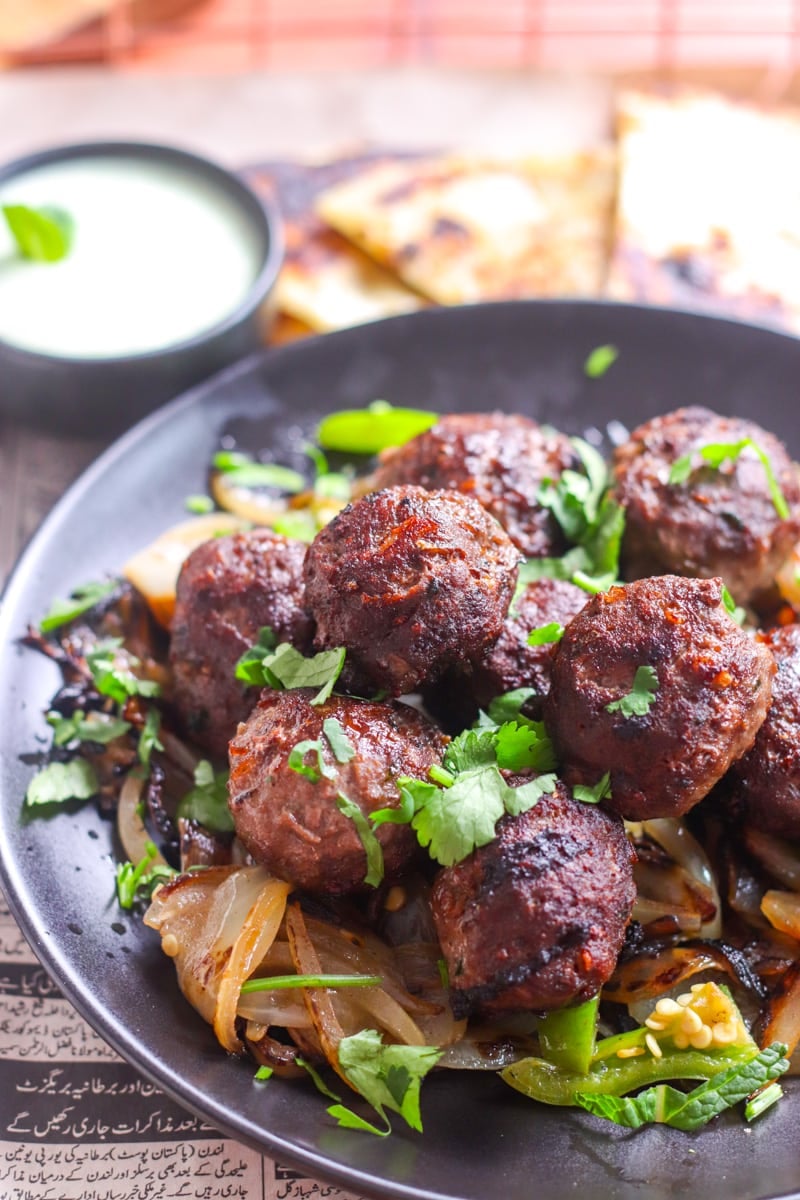 ¾ view of a plate of gola kabab garnished with cilantro, paratha and chutney in the background