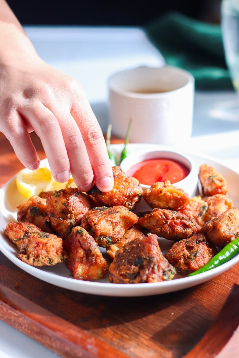 a hand reaching for a chicken pakora