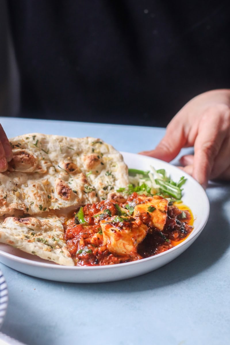 fish karahi on a table with naan and a hand showing