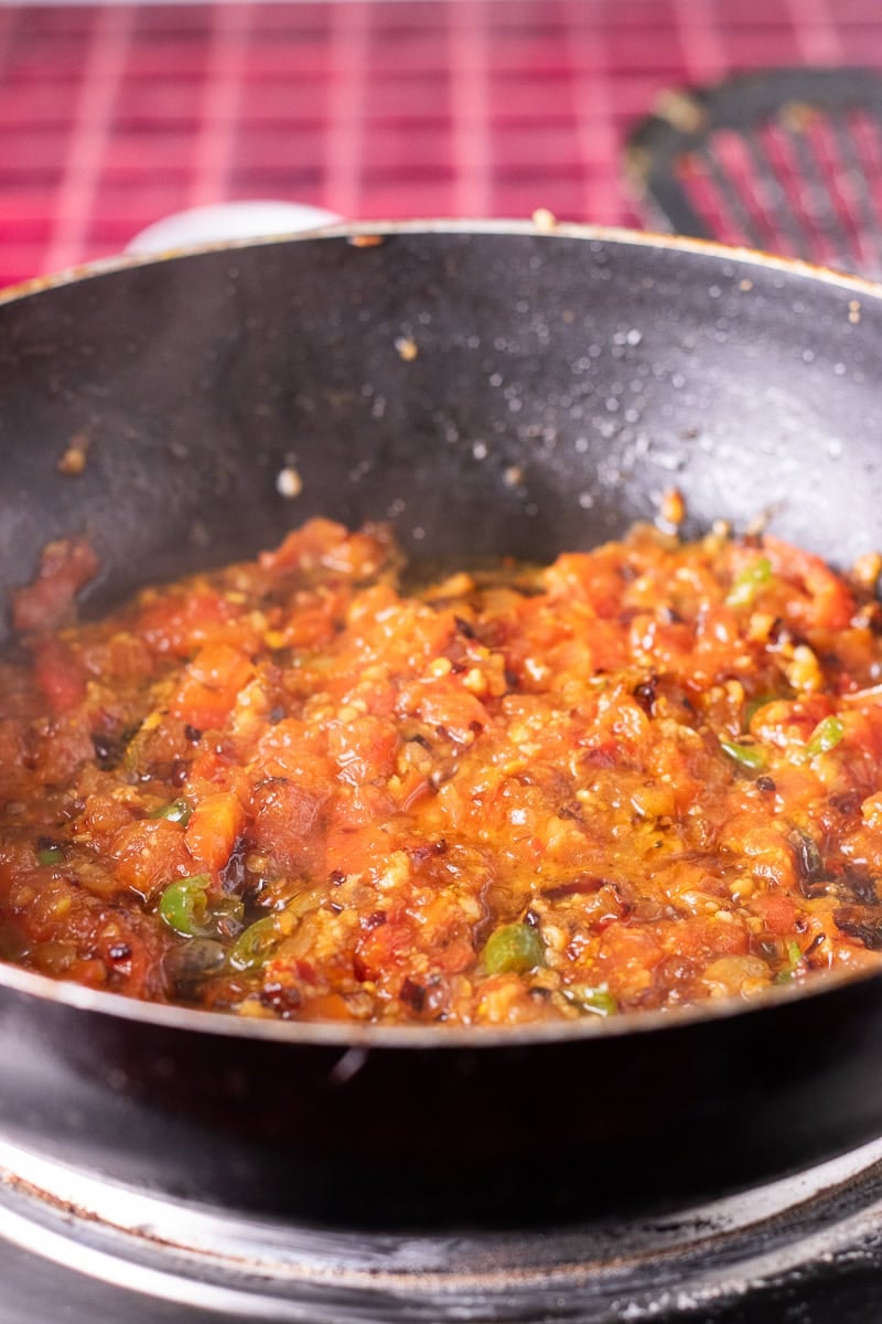 tomatoes added and being sauteed in a wok for the base of palak paneer