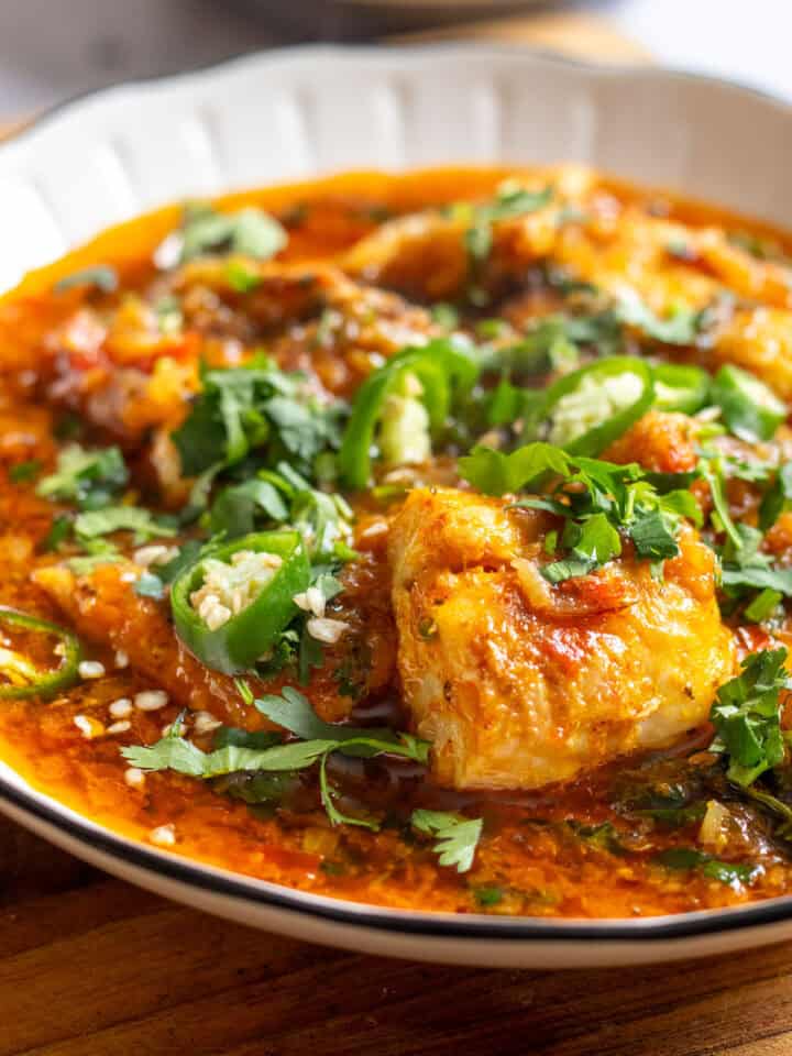 a bowl of fish curry garnished with fresh coriander and chilies
