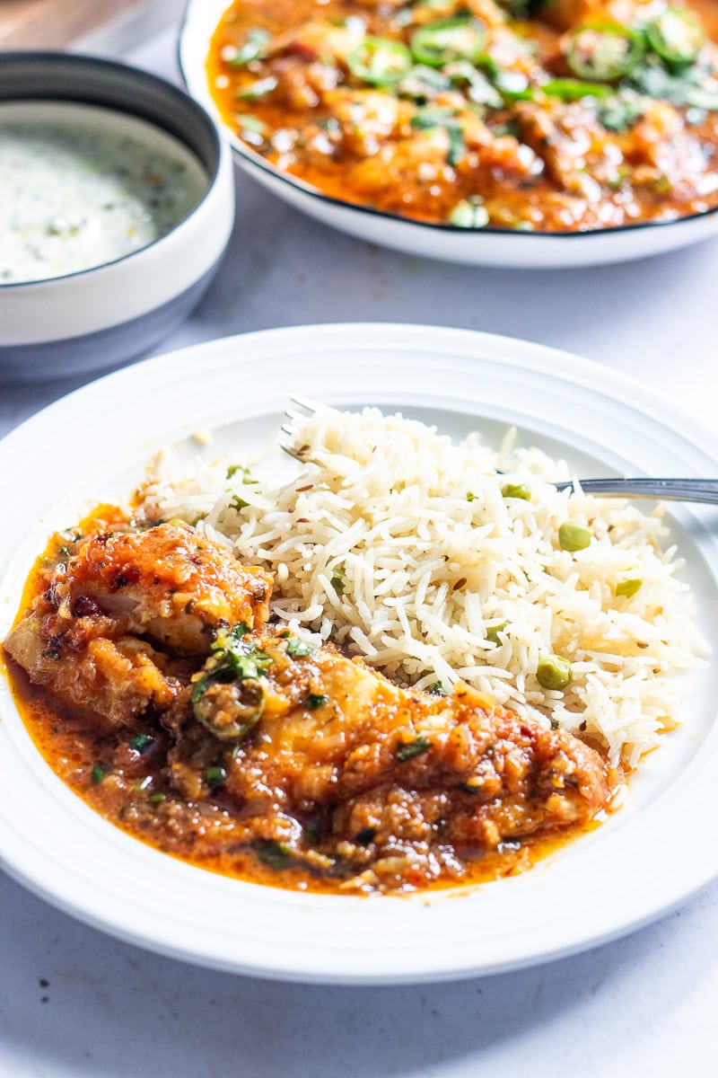 fish ka salan with a pea pilaf in the foreground, a bowl of raita and the dish for the fish curry in the background