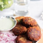 a plate of shami kabab with onions, a green raita/chutney and cilantro in a jar in the background