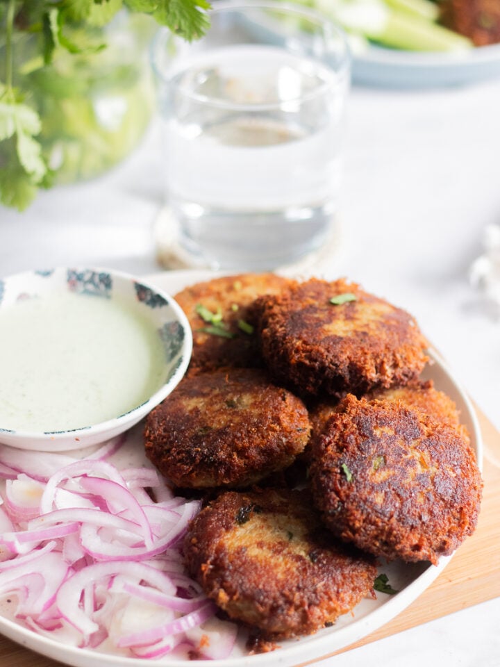 a plate of shami kabab with onions, a green raita/chutney and cilantro in a jar in the background