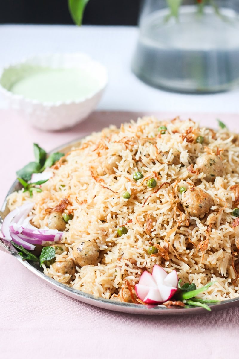 a plate of moti pulao with raita and a dish of it in the background
