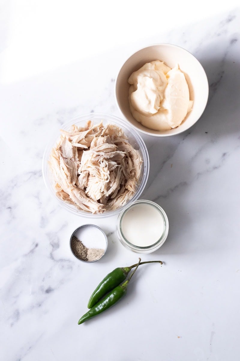 top down view of chicken sandwich ingredients - mayo, shredded chicken, cream, salt, pepper, white pepper and green chilies