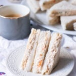 creamy bakery style mayo chicken sandwiches on a plate, cup of tea and a platter of sandwiches in the background