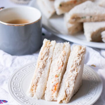 creamy bakery style mayo chicken sandwiches on a plate, cup of tea and a platter of sandwiches in the background
