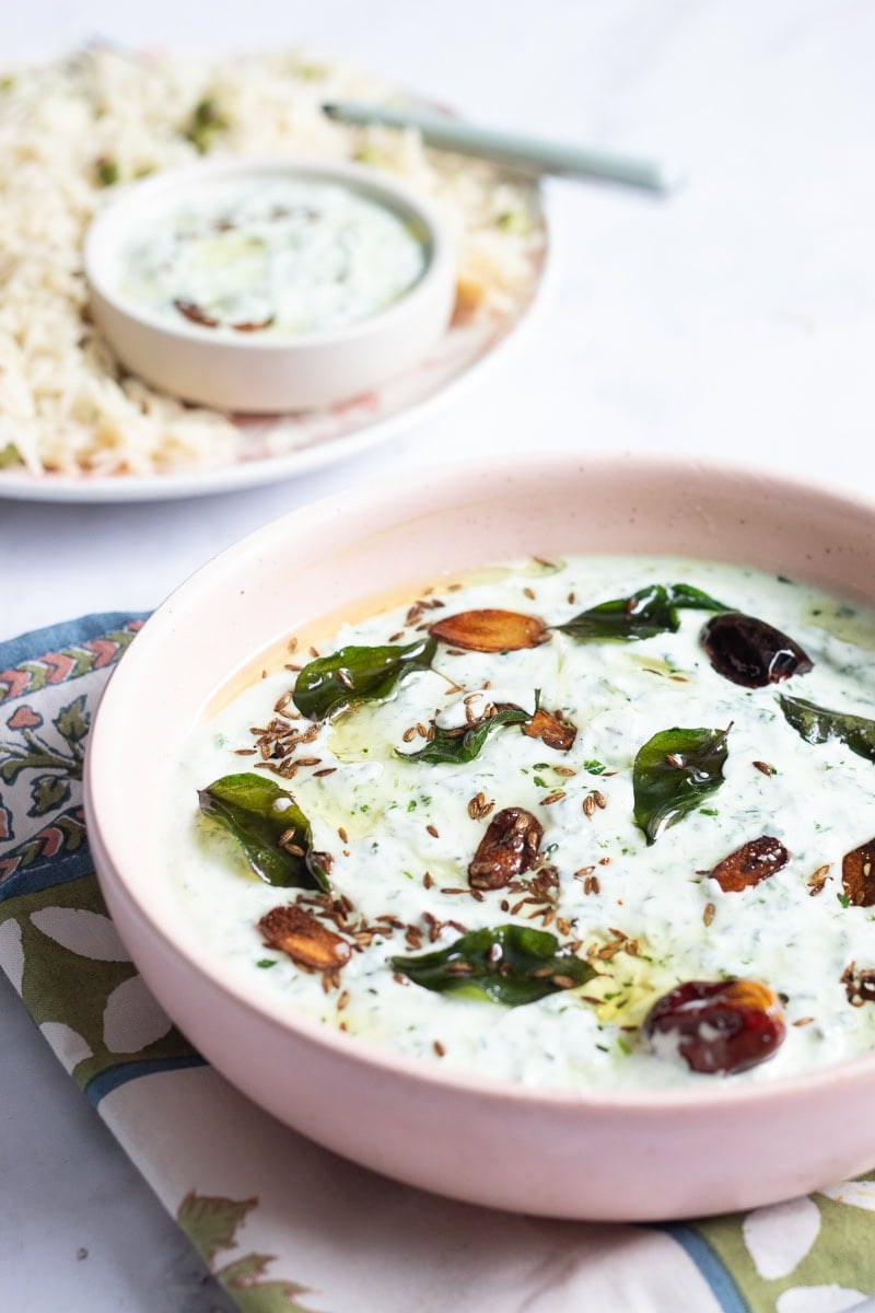 ¾ view of a raita bowl, rice in the background with more raita