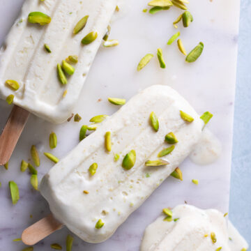 pista kulfi on a marble board with pistachios scattered over top